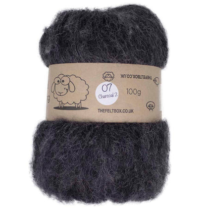 A carded wool batt in charcoal color, packaged in a brown paper wrap with a label that includes the brand name 'The Felt Box' and the weight of 100 grams.