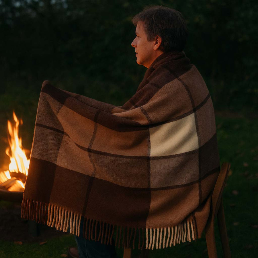 Person wrapped in a plaid blanket by a campfire in a dark outdoor setting