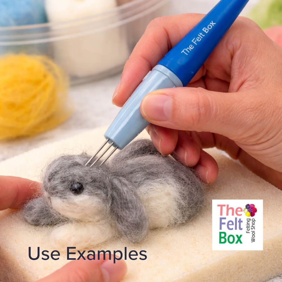 Hands using a three-needle felting pen to shape a small needle felted bunny on a light blue felting sponge, showing the multi-needle tool in use for surface shaping and detailing.