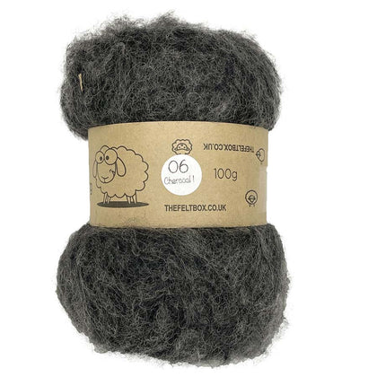A carded wool batt in charcoal color, packaged in a brown paper wrapping with a label that indicates it is 100% sheep wool from The Felt Box, weighing 100g.
