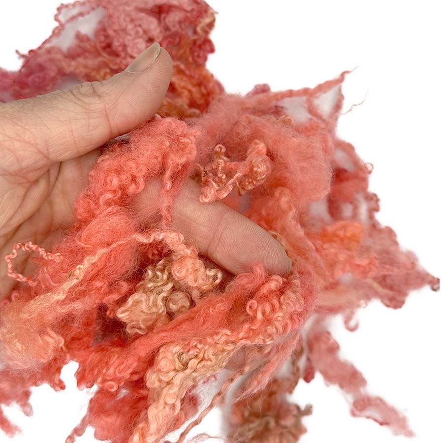 Hand holding pinkish-orange fluffy locks bfl against a white background