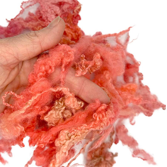 Hand holding pinkish-orange fluffy locks bfl against a white background