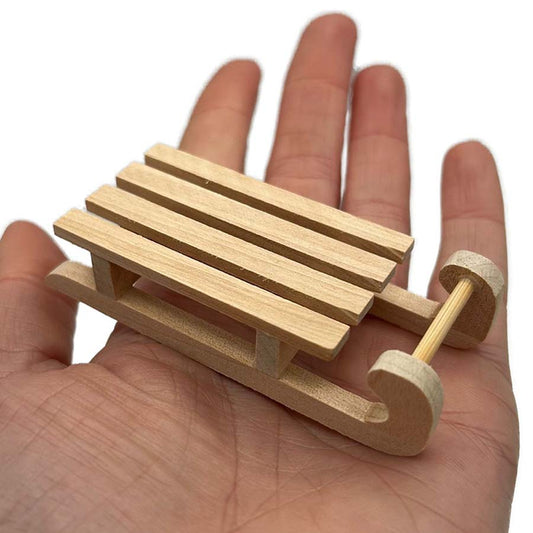 Hand holding a small wooden sledge, showing size and detail of 65mm miniature sled for needle felting scenes and craft projects