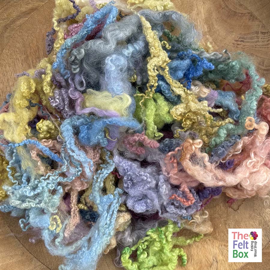 Colorful felted wool fibers on a wooden surface with 'The Felt Box' branding.
