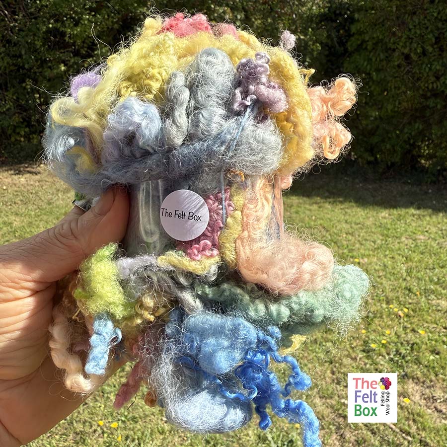 Curly hand-dyed British wool locks – perfect for needle felting, art yarn, and fibre projects. Wensleydale & BFL curls, dyed in rich colours. 50g pack held againsg green baclkgrungd in bright light