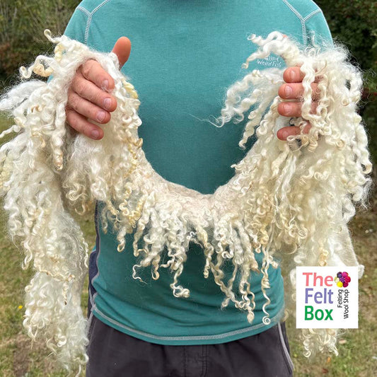 Person holding a white curly scarf with 'The Felted Box' logo in the corner.