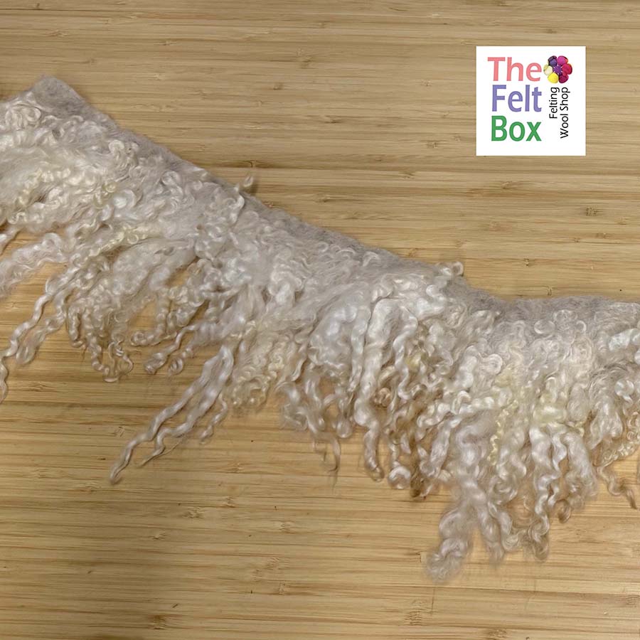 Fringe fabric on a wooden surface with 'The Felt Box' logo.