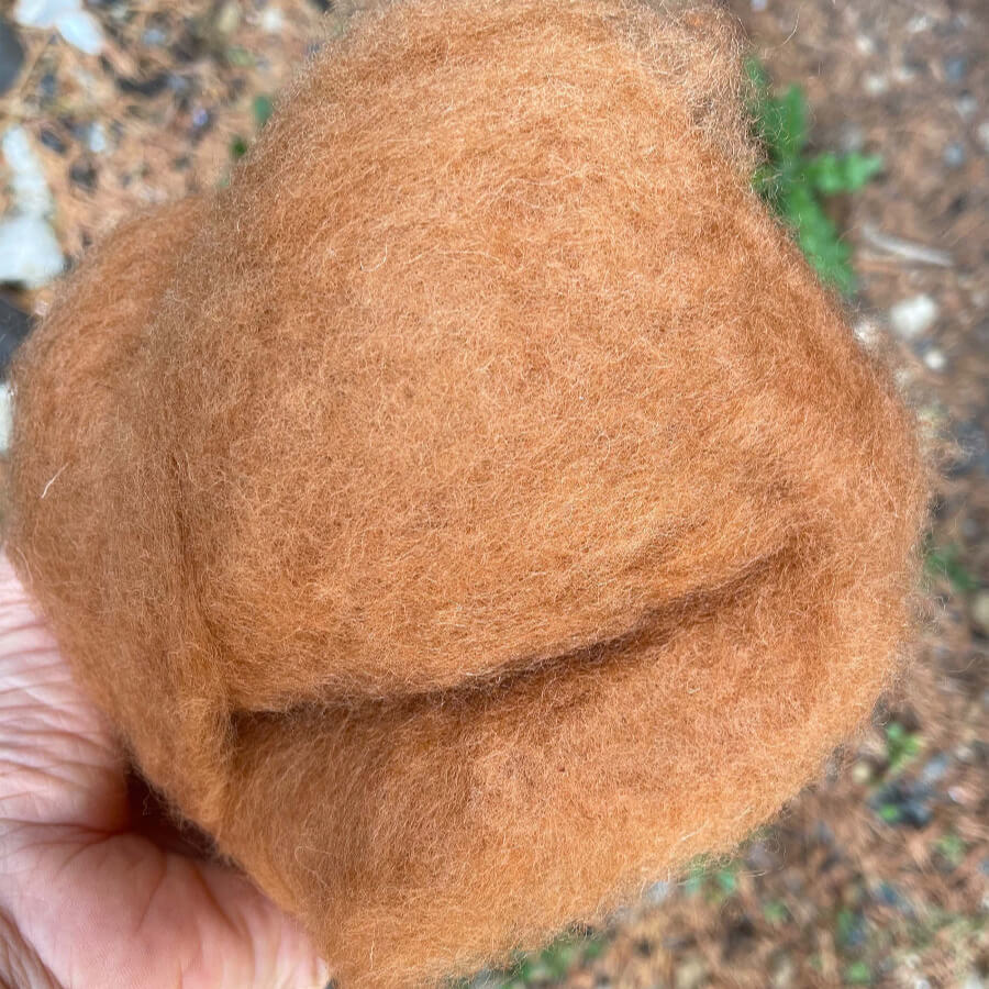 brown ginger carded wool for needle felting hold in hand against natural stone background to show colour. 
